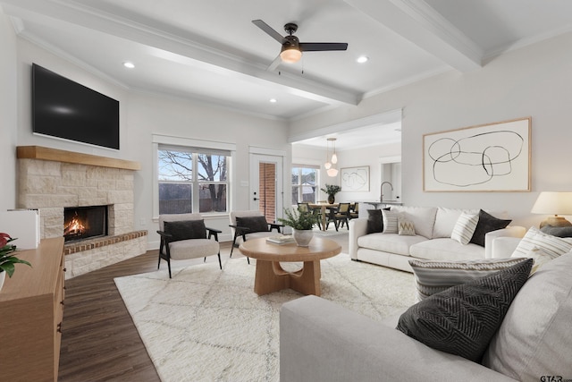 living room featuring crown molding, dark wood-type flooring, ceiling fan, beam ceiling, and a fireplace