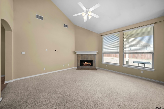 unfurnished living room with a tiled fireplace, carpet floors, high vaulted ceiling, and ceiling fan