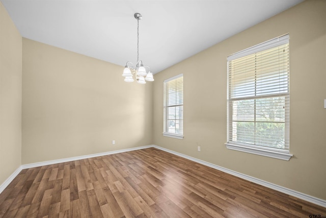 spare room featuring wood-type flooring and a notable chandelier