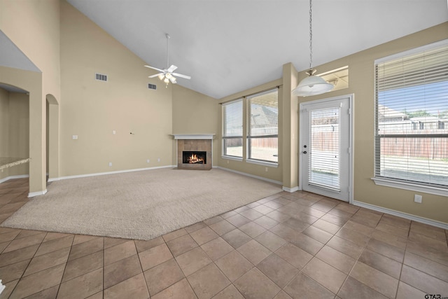 unfurnished living room featuring a tiled fireplace, high vaulted ceiling, light colored carpet, and ceiling fan