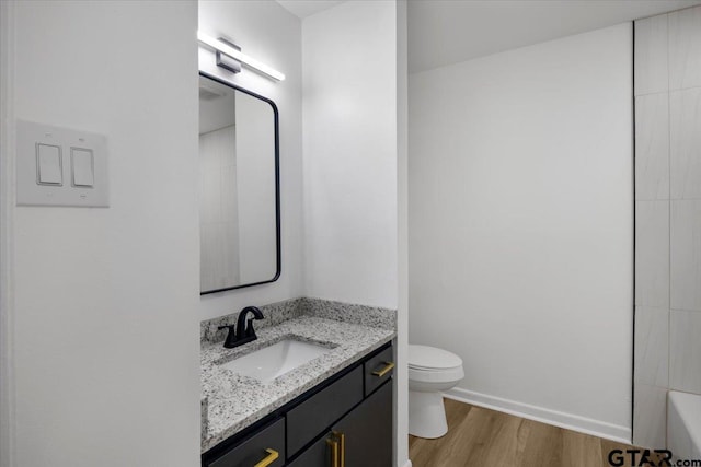 full bath with vanity, wood finished floors, toilet, baseboards, and a tub to relax in