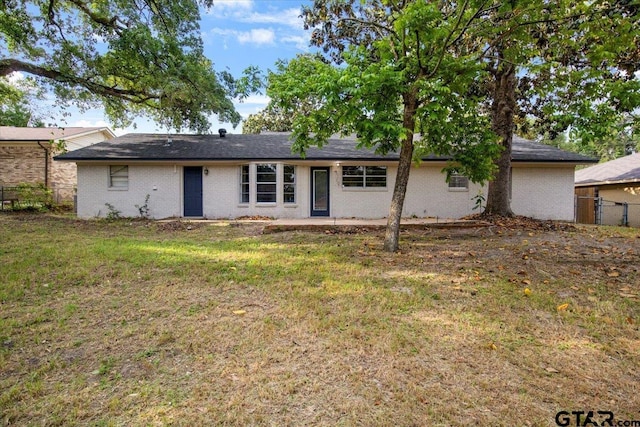 single story home with brick siding, fence, a shingled roof, and a front lawn