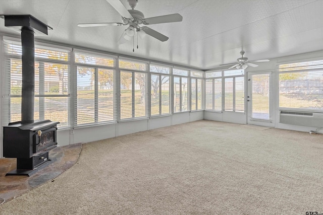 unfurnished sunroom featuring ceiling fan, a wood stove, and cooling unit
