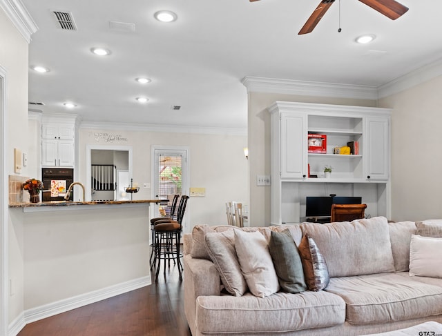 living room featuring ceiling fan, built in desk, dark hardwood / wood-style floors, and ornamental molding