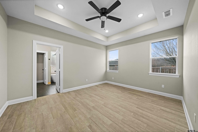 unfurnished bedroom featuring connected bathroom, light wood-type flooring, a tray ceiling, and ceiling fan