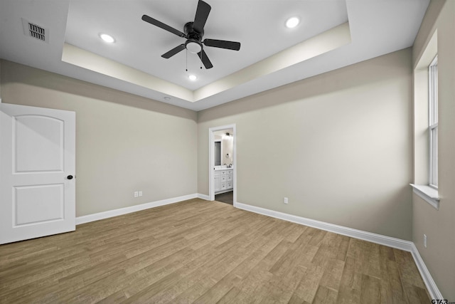 unfurnished bedroom with light hardwood / wood-style floors, ceiling fan, and a raised ceiling