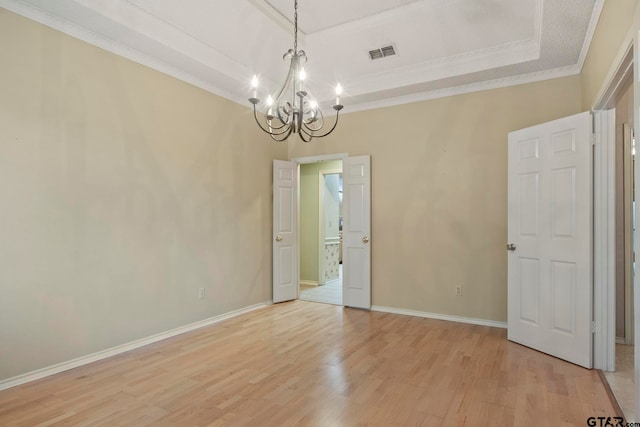 unfurnished room featuring a raised ceiling, light hardwood / wood-style flooring, a notable chandelier, and crown molding