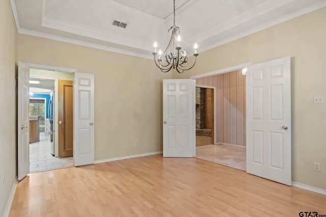 empty room with light hardwood / wood-style floors, a raised ceiling, an inviting chandelier, and crown molding