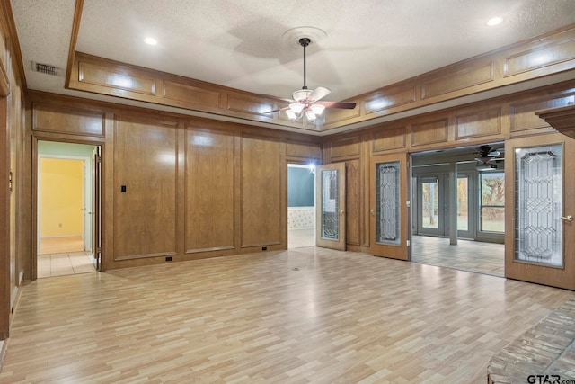 empty room featuring wooden walls, a textured ceiling, ceiling fan, and light hardwood / wood-style flooring