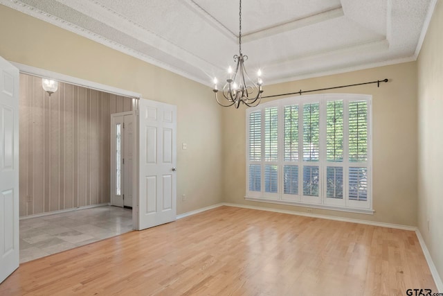 spare room with ornamental molding, a textured ceiling, an inviting chandelier, a tray ceiling, and wood-type flooring