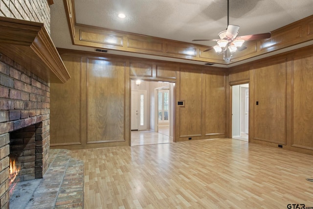 unfurnished living room featuring a brick fireplace, light wood-type flooring, wood walls, and a textured ceiling