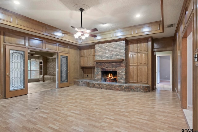 unfurnished living room featuring a brick fireplace, ceiling fan, a textured ceiling, and light wood-type flooring