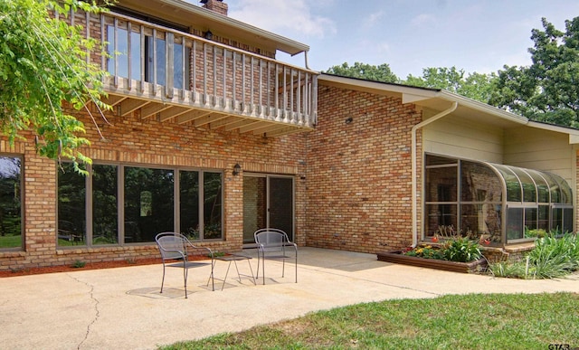 back of property featuring a sunroom, a balcony, and a patio