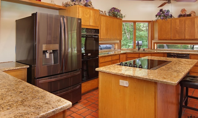 kitchen with a kitchen breakfast bar, light stone counters, ceiling fan, sink, and black appliances