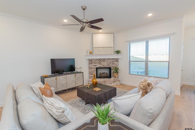 living room with a fireplace, light hardwood / wood-style floors, ceiling fan, and crown molding