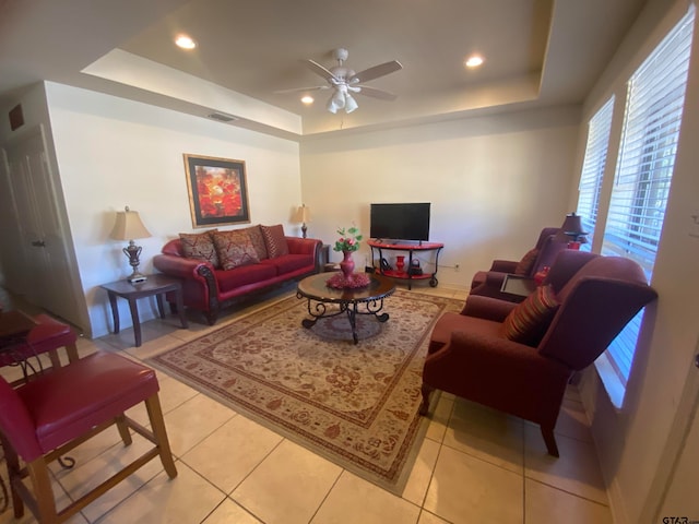 living room featuring ceiling fan, a tray ceiling, and light tile patterned flooring