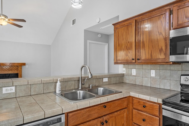 kitchen featuring visible vents, lofted ceiling, brown cabinets, stainless steel appliances, and a sink