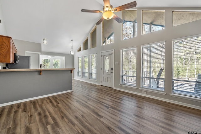 unfurnished living room featuring high vaulted ceiling, dark wood finished floors, a ceiling fan, and baseboards