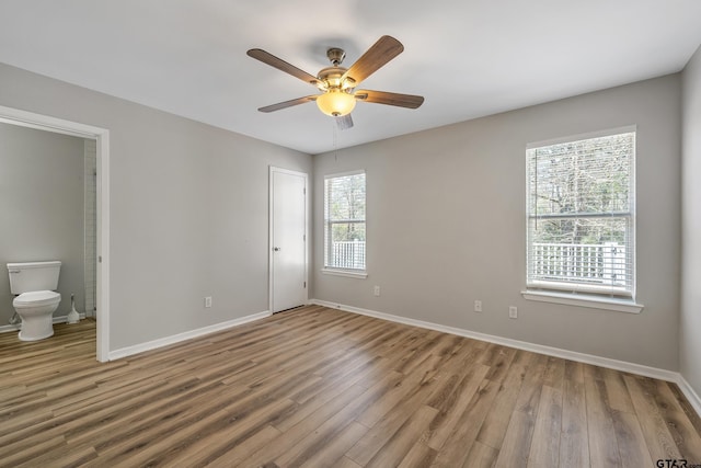 unfurnished bedroom with wood finished floors, connected bathroom, and baseboards