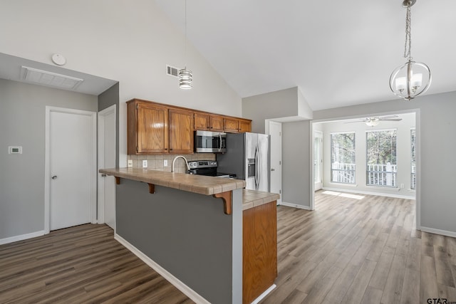 kitchen featuring stainless steel appliances, a peninsula, visible vents, tile counters, and brown cabinets