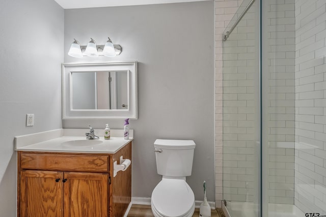 bathroom featuring toilet, a stall shower, baseboards, and vanity