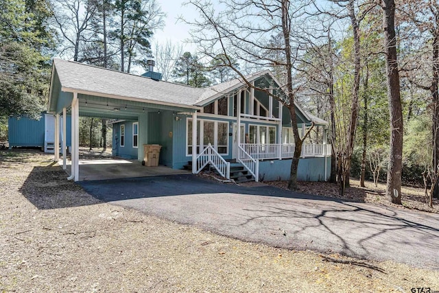 chalet / cabin with driveway, an attached carport, an outdoor structure, and roof with shingles