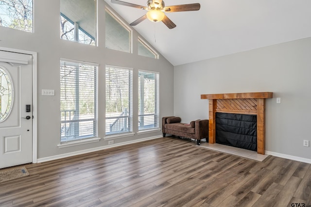 interior space featuring baseboards, a ceiling fan, wood finished floors, a fireplace, and high vaulted ceiling