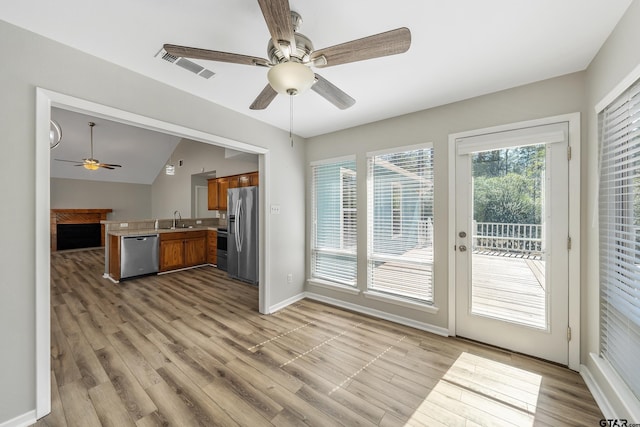 kitchen with brown cabinetry, open floor plan, a peninsula, stainless steel appliances, and a sink