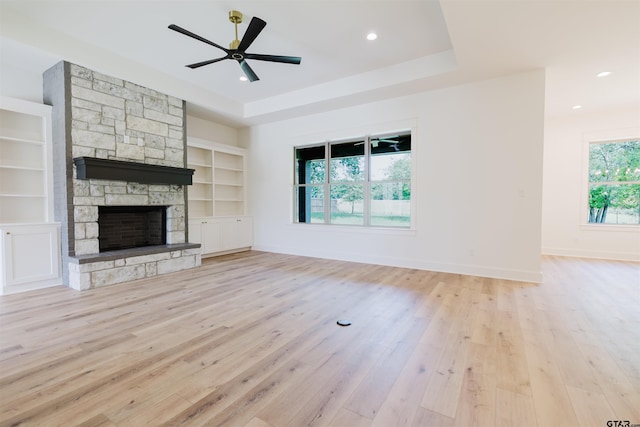 unfurnished living room featuring built in features, baseboards, light wood-type flooring, and a stone fireplace
