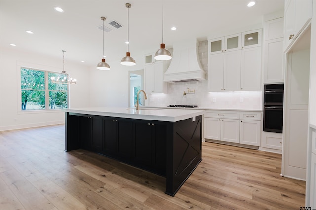 kitchen featuring dobule oven black, decorative backsplash, custom exhaust hood, light countertops, and a sink