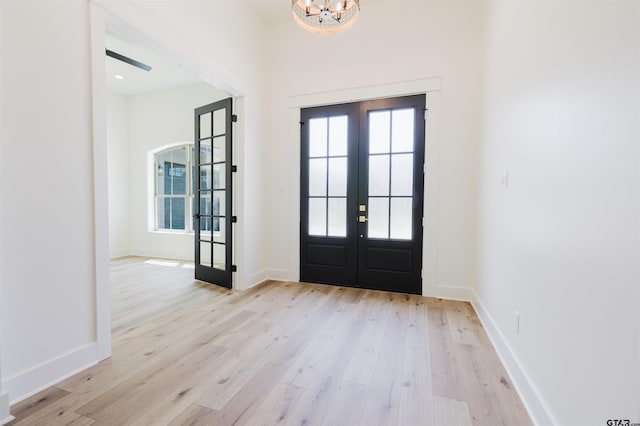 foyer with baseboards, a notable chandelier, french doors, and light wood finished floors