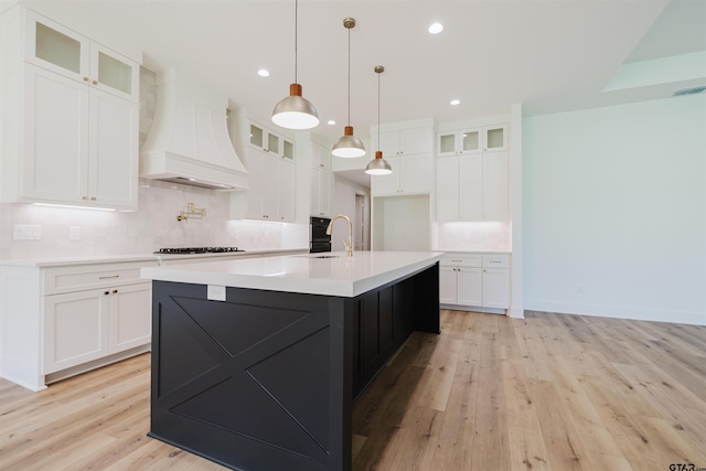 kitchen with light countertops, light wood-style flooring, custom exhaust hood, and tasteful backsplash