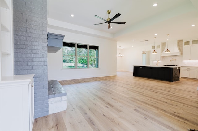 unfurnished living room featuring a sink, ceiling fan with notable chandelier, recessed lighting, light wood-type flooring, and a tray ceiling