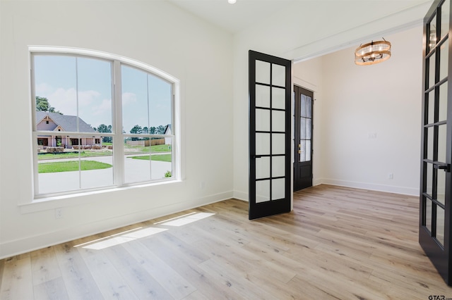 empty room with french doors, light wood-style floors, baseboards, and a chandelier
