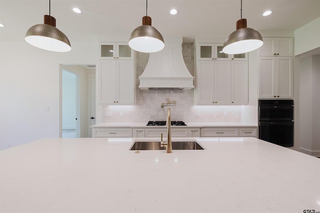 kitchen with dobule oven black, custom exhaust hood, gas cooktop, white cabinets, and backsplash