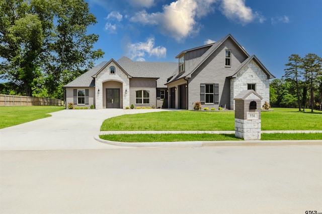 french country inspired facade with board and batten siding, fence, a front lawn, concrete driveway, and stone siding
