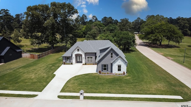 view of front of property featuring fence, concrete driveway, a front lawn, and stone siding