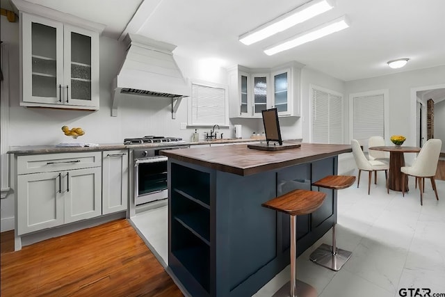 kitchen with wood counters, custom exhaust hood, sink, range, and a kitchen island