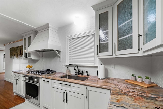 kitchen with appliances with stainless steel finishes, light wood-type flooring, custom exhaust hood, sink, and white cabinetry