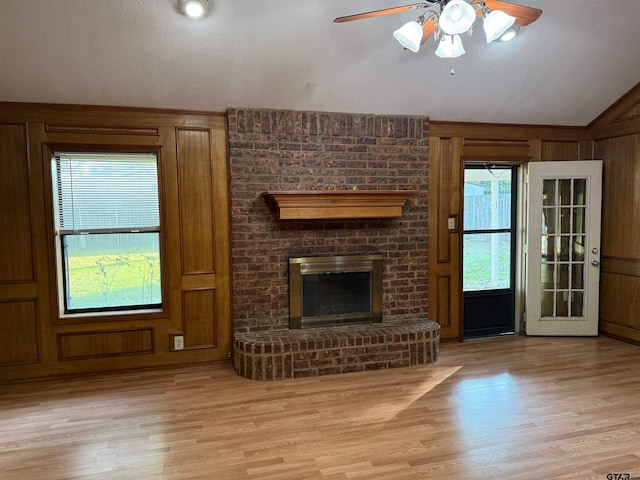 unfurnished living room featuring light wood-type flooring, a fireplace, wooden walls, and vaulted ceiling