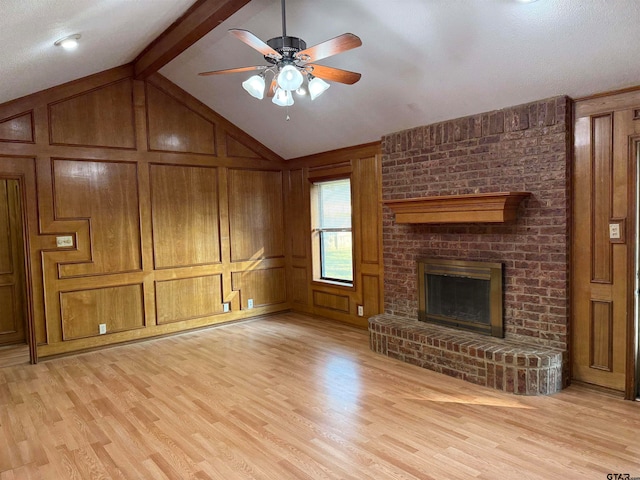 unfurnished living room with wood walls, a fireplace, ceiling fan, lofted ceiling with beams, and light hardwood / wood-style flooring