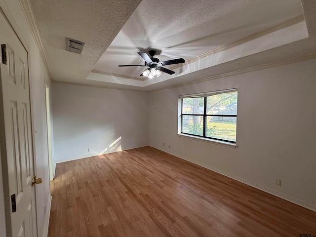 spare room featuring ornamental molding, ceiling fan, a textured ceiling, a raised ceiling, and light hardwood / wood-style flooring