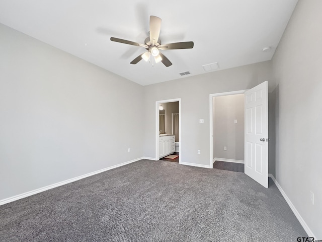 unfurnished bedroom with ceiling fan, ensuite bathroom, and dark colored carpet