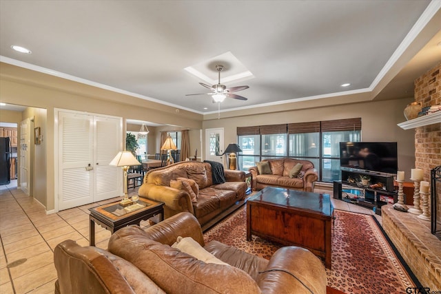 living room with light tile patterned flooring, a fireplace, crown molding, a tray ceiling, and ceiling fan