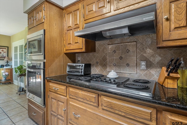 kitchen with dark stone counters, light tile patterned flooring, ventilation hood, backsplash, and appliances with stainless steel finishes