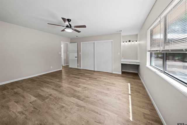 unfurnished bedroom with hardwood / wood-style floors, built in desk, and ceiling fan