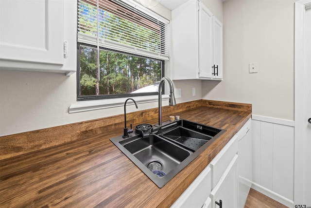 kitchen with butcher block counters, wood-type flooring, sink, and white cabinets