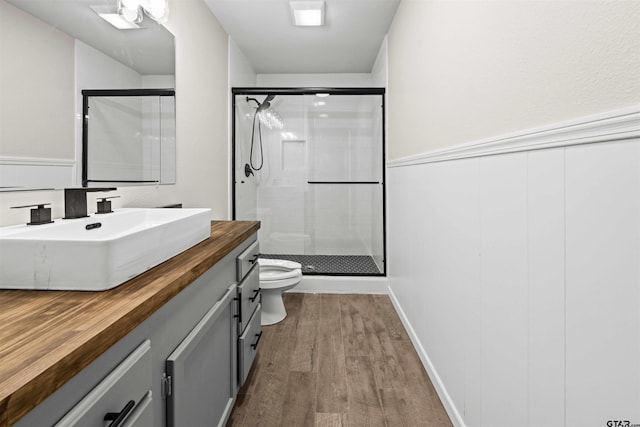 bathroom with hardwood / wood-style floors, walk in shower, vanity, and toilet