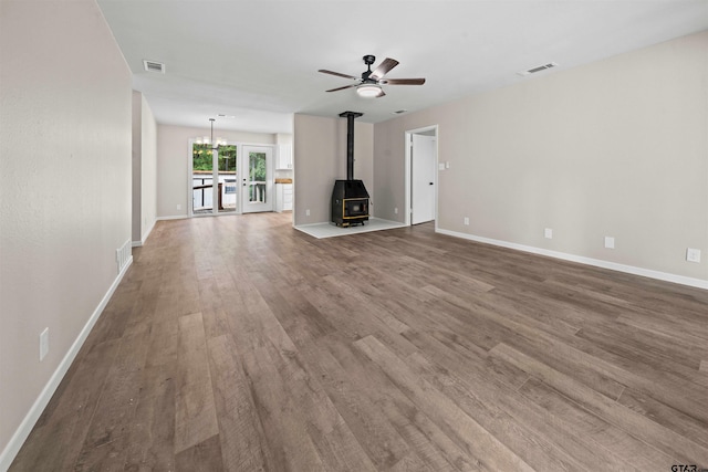 unfurnished living room with a wood stove, hardwood / wood-style floors, and ceiling fan with notable chandelier