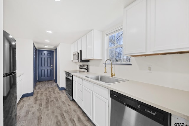 kitchen featuring stainless steel appliances, a sink, white cabinetry, light countertops, and light wood-type flooring